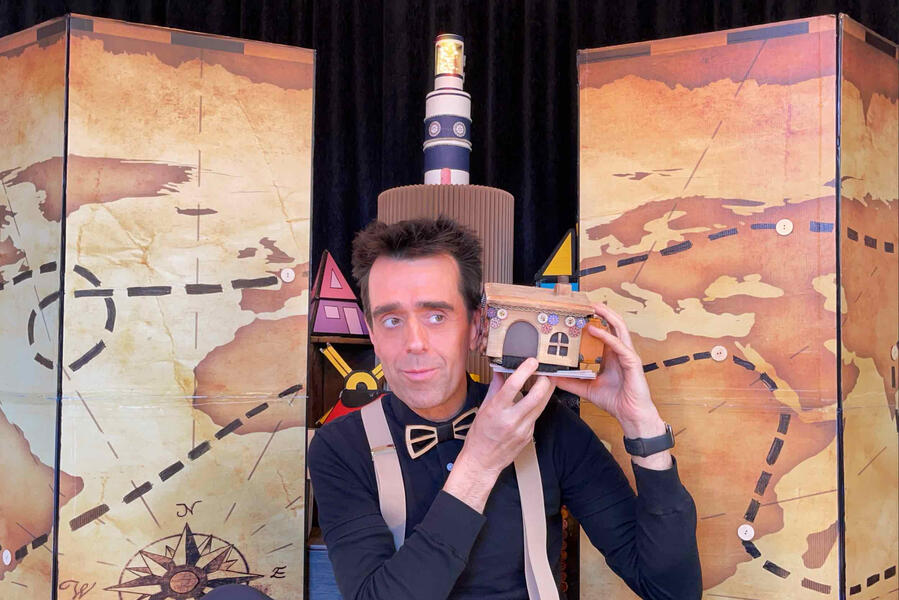 Risque-Tout Monsieur Fred, devant son décor, représentant une carte géante et le village avec toutes les petites maisons devant un jeune public en Île-de-France